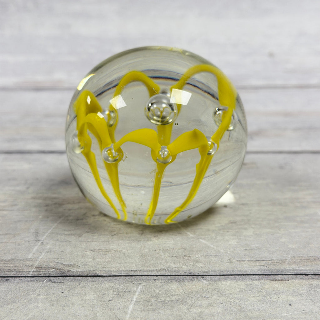 Clear glass paperweight with bright yellow ribbon loops and controlled bubbles
