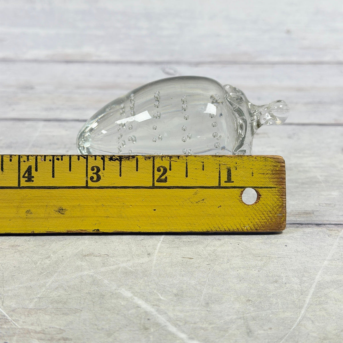 Clear strawberry-shaped glass paperweight with controlled bubbles, shown beside ruler