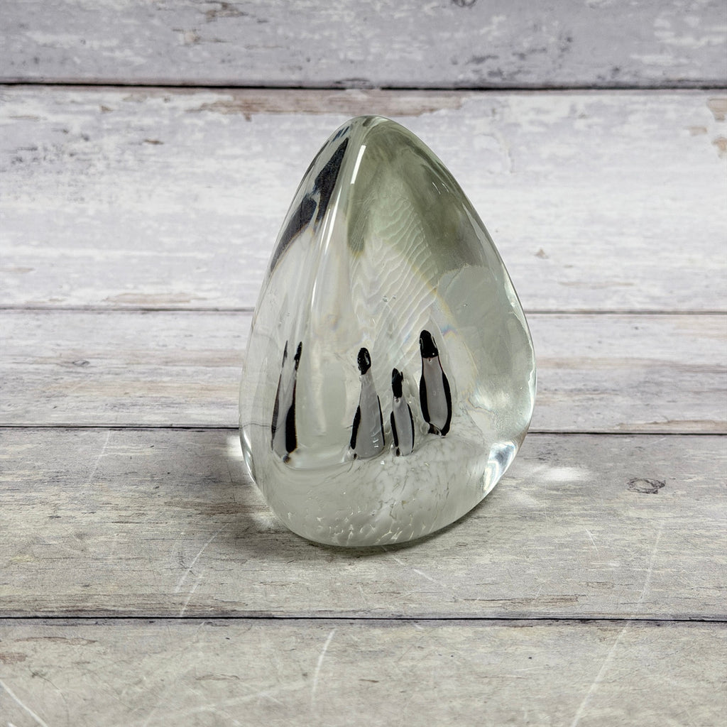 Clear teardrop glass paperweight with four black-and-white penguins in a snowy white scene