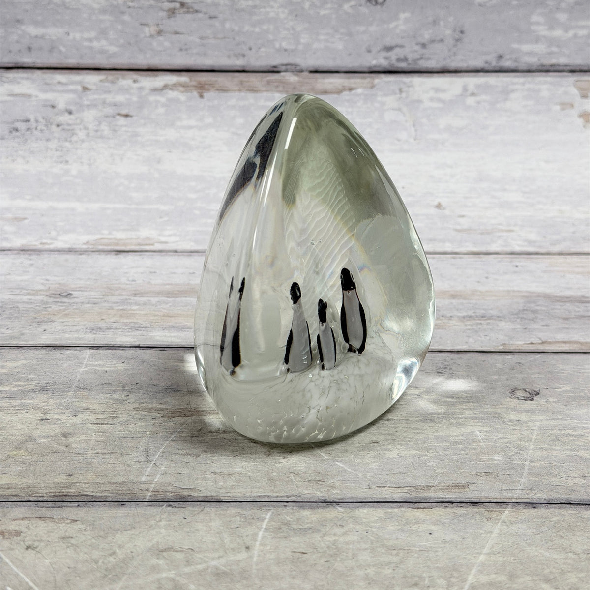 Clear teardrop glass paperweight with four black-and-white penguins in a snowy white scene