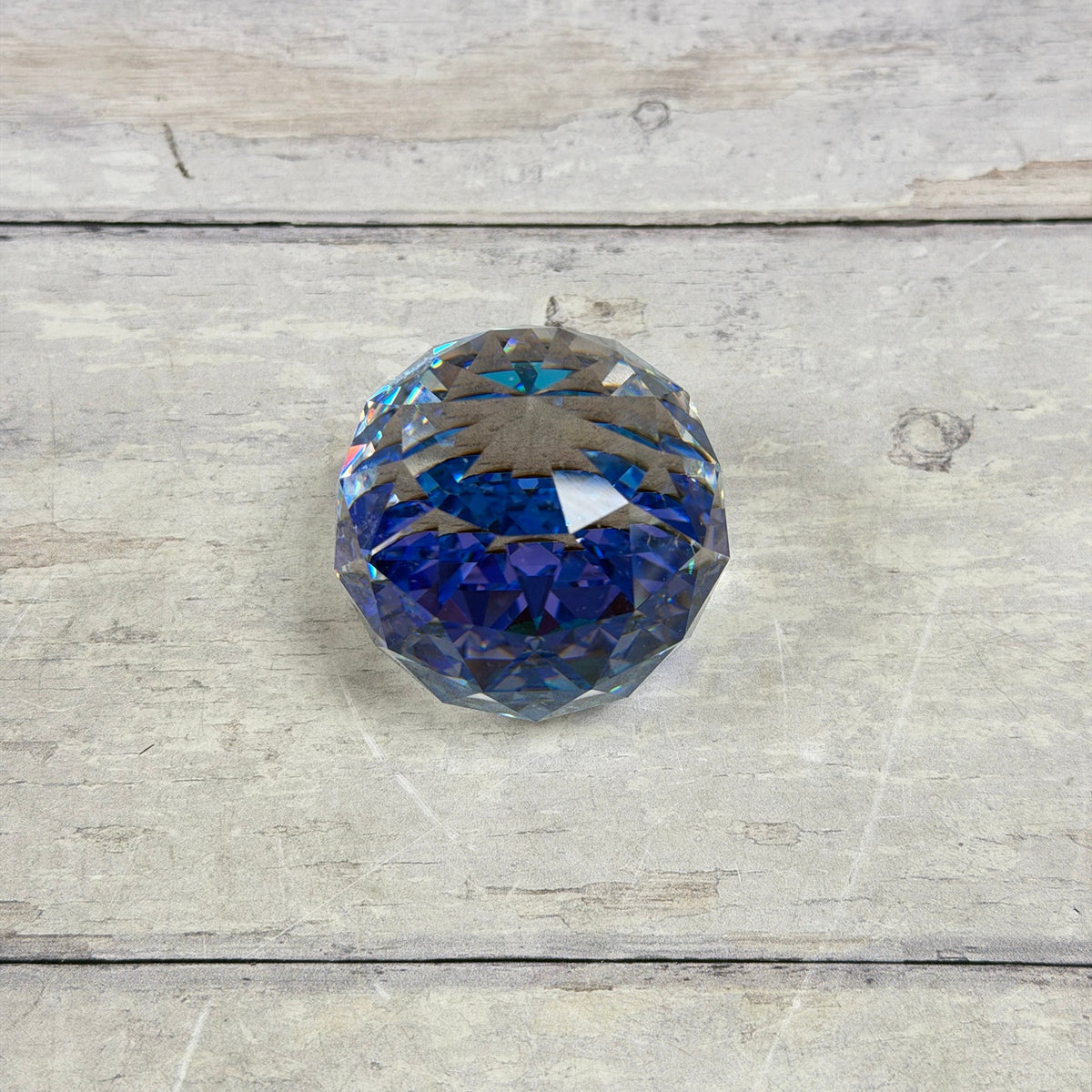 Top view of clear faceted glass paperweight showing a geometric star-like arrangement and blue-purple reflections